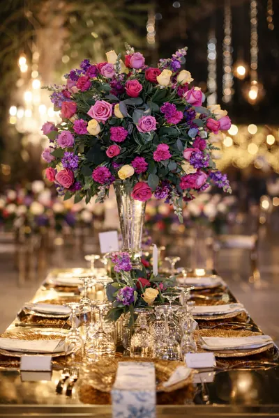 Centro de mesa alto de rosas fucsia, moradas y blancas en jarrón de cristal