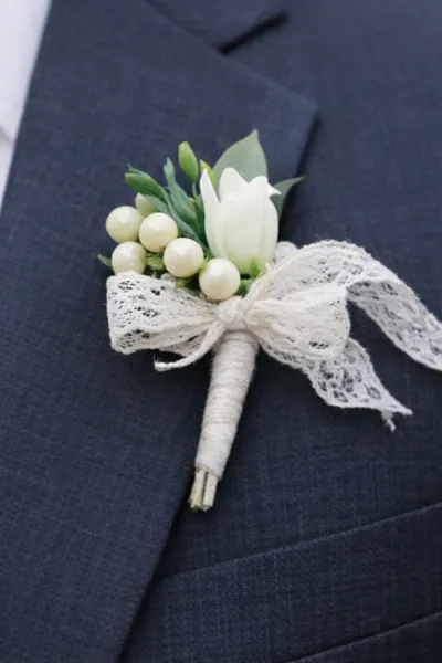 Boutonnière de capullo blanco y bayas perladas con lazo de encaje en un traje azul oscuro
