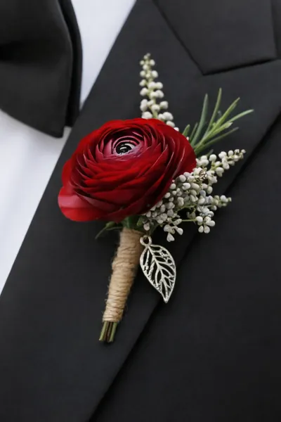 Boutonnière de ranúnculo rojo con flores blancas y hoja dorada en un esmoquin negro