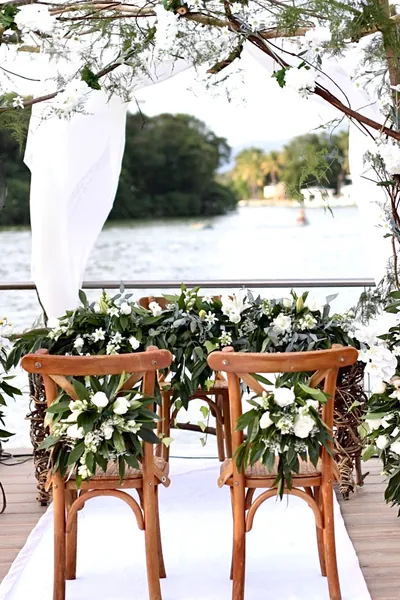 Ceremonia junto al lago con sillas de los novios y arreglos de flores blancas